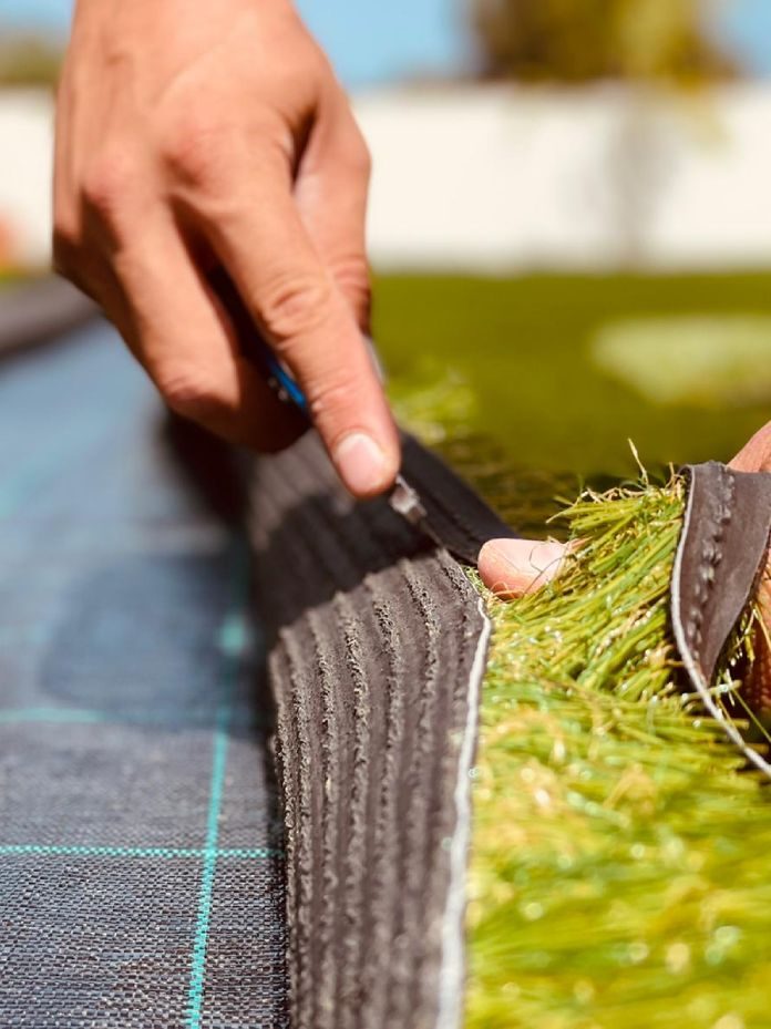 Instalador de Flor & Design cortando un rollo de césped artificial durante la instalación